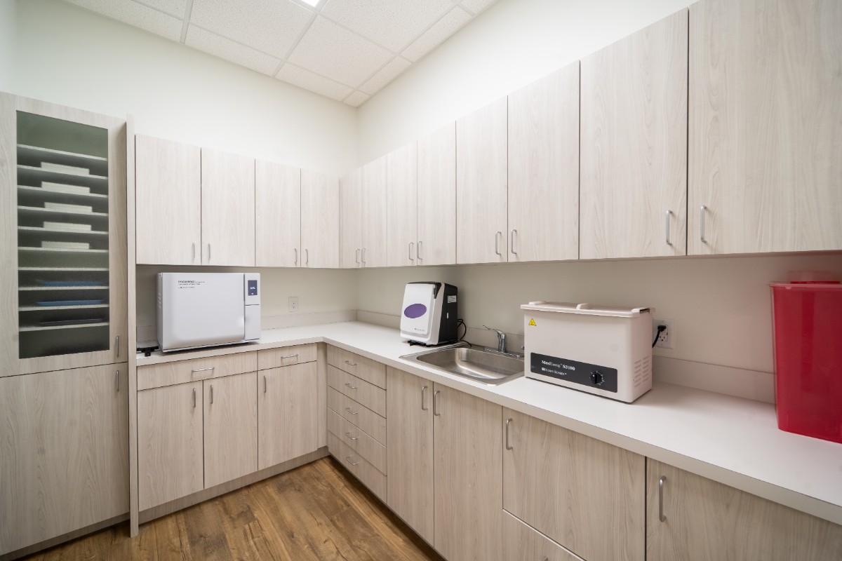 Clean medical sterilization room with wooden cabinets, countertop, sink, and various sterilization machines.