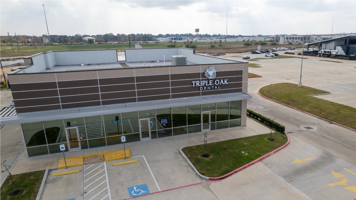Exterior view of a single-story commercial building with a sign reading 'Triple Oak Dental' and an empty parking lot with handicap spaces.