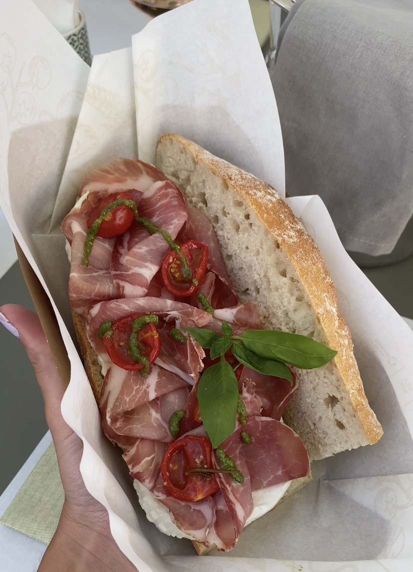 Sandwich with layers of deli meats and lettuce cut in half on white paper next to an open can of Diet Coke.