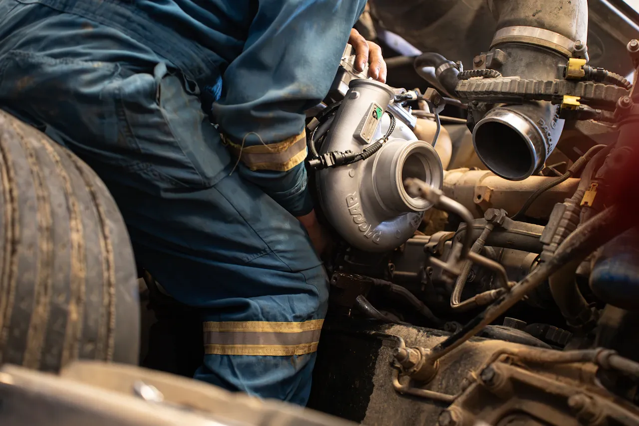 Exhaust system repair on a heavy-duty truck as a technician installs a turbocharger, with intake piping and engine components exposed for service.