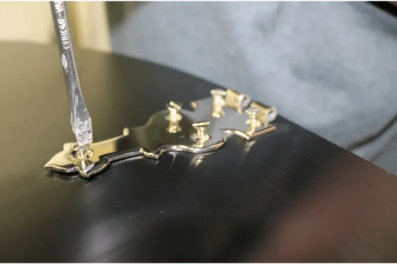 A person uses a screwdriver to adjust a tuning machine on a guitar headstock, akin to how experts fine-tune the exquisite details in Steinway Restorations.