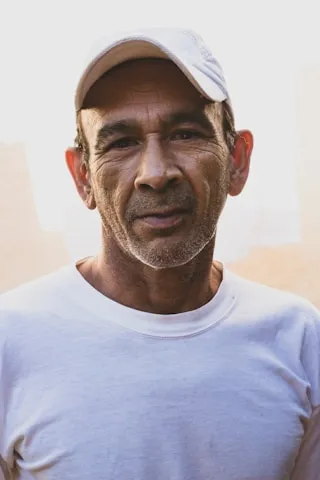 A man in a white cap and t-shirt stands poised before a neutral backdrop.
