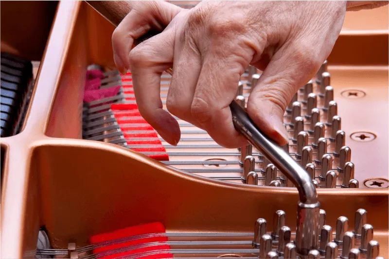 A person's hand carefully tunes the strings of a piano with a tuning lever, ensuring each note resonates perfectly.