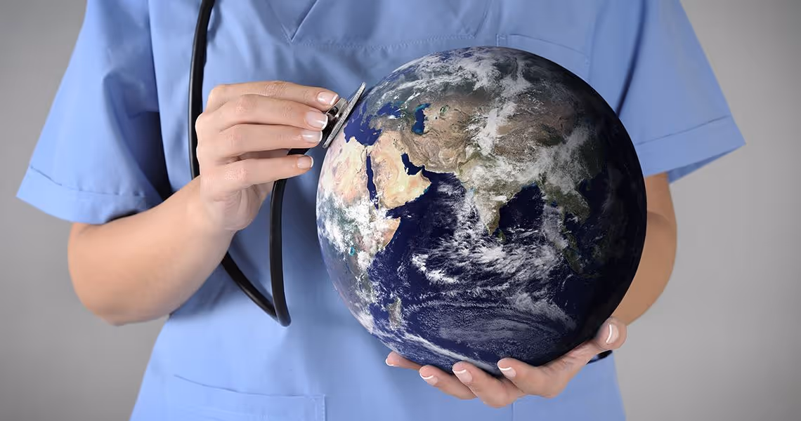 Healthcare professional in blue scrubs holding a globe and using a stethoscope to listen to it.