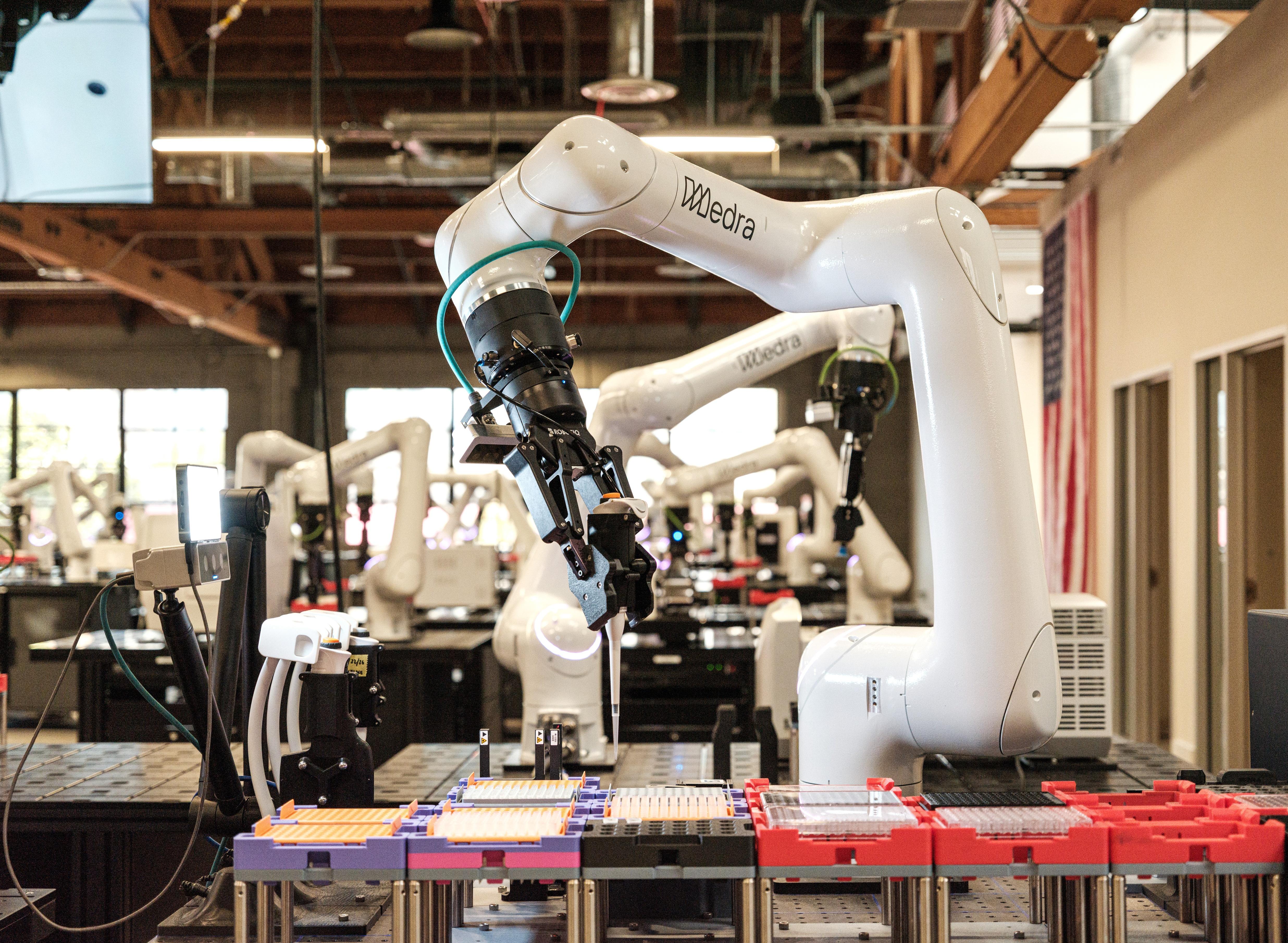 Close-up of white robotic arms with the label 'Medra' in a dimly lit industrial setting.