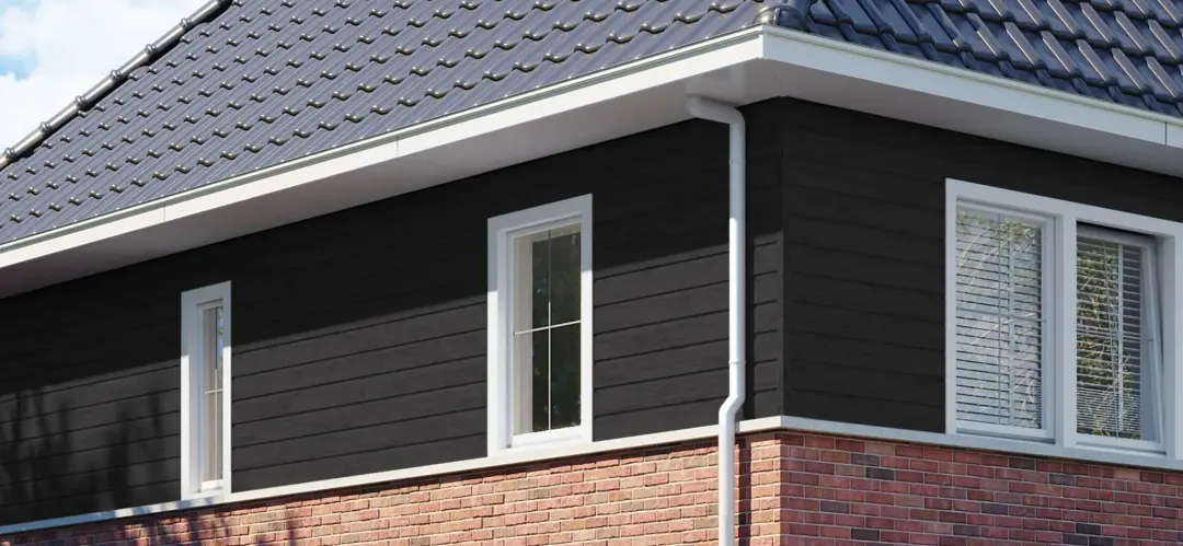 Donkere gevelbekleding met een wit kunststof raam aan de zijgevel van een woning