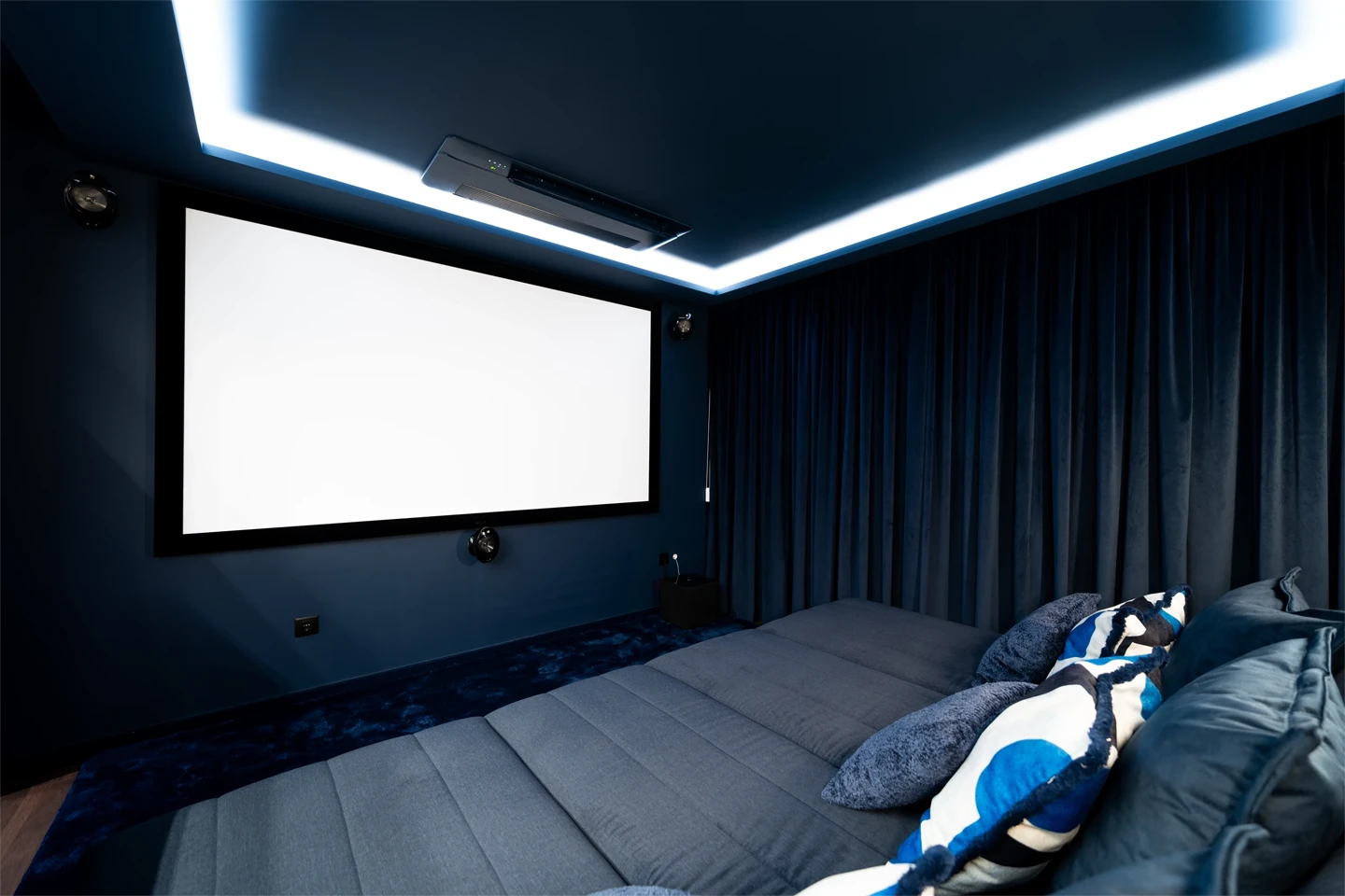 Sala de estar moderna com sofá bege, mesa de centro escura com livros e xícara, TV embutida na parede e vasos decorativos com galhos secos.