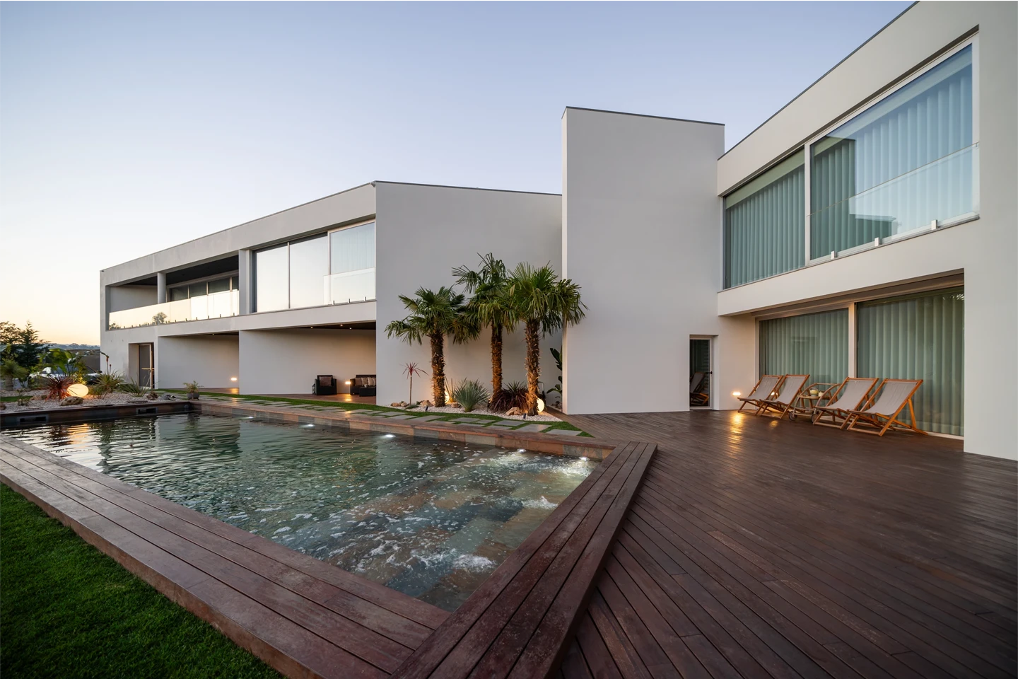 Sala de estar moderna com sofá claro, mesa de centro espelhada, grandes janelas de vidro e vista para área externa com lounge e piscina.
