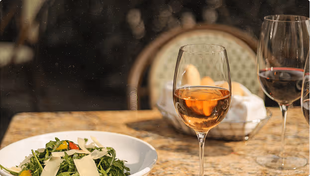 Mesa con una ensalada en un plato blanco y dos copas de vino, una con vino rosado y otra con vino tinto.
