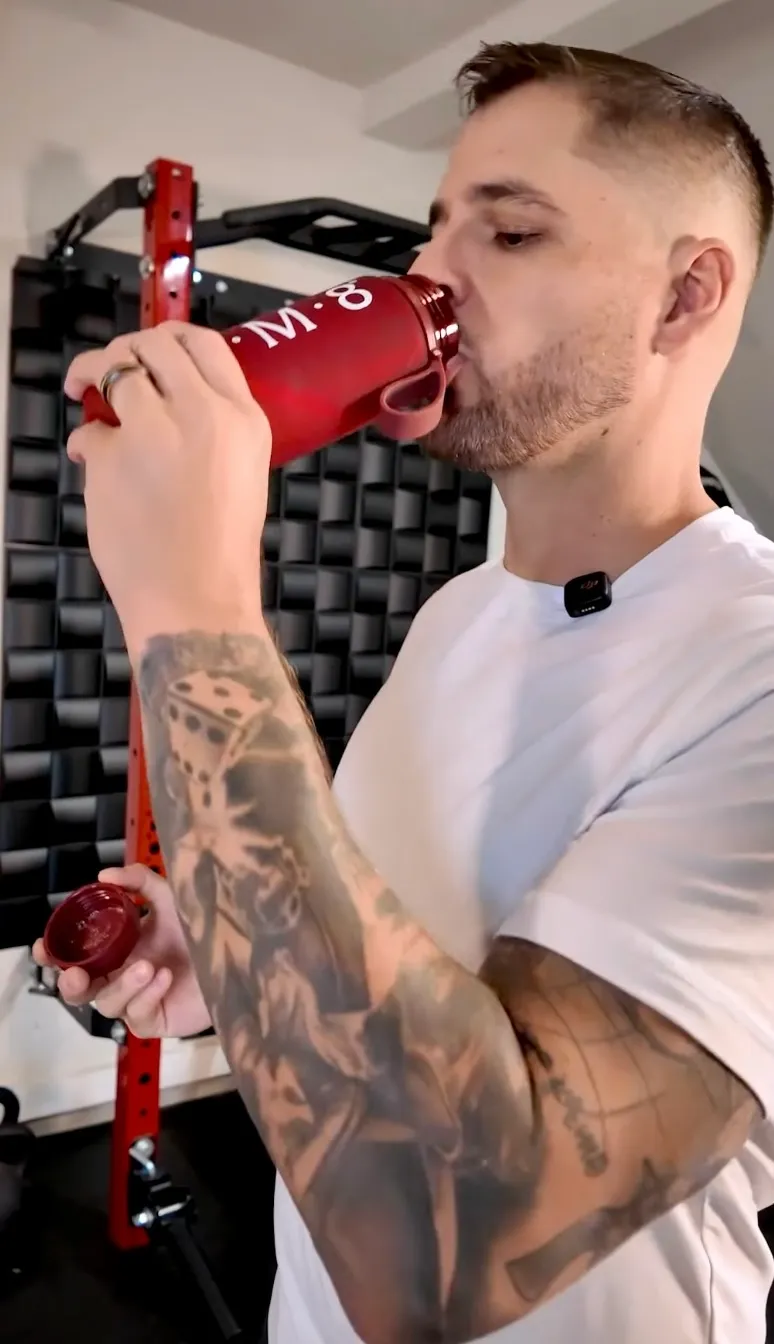 Tyler Lesher drinking from an IM8 bottle in a home gym.