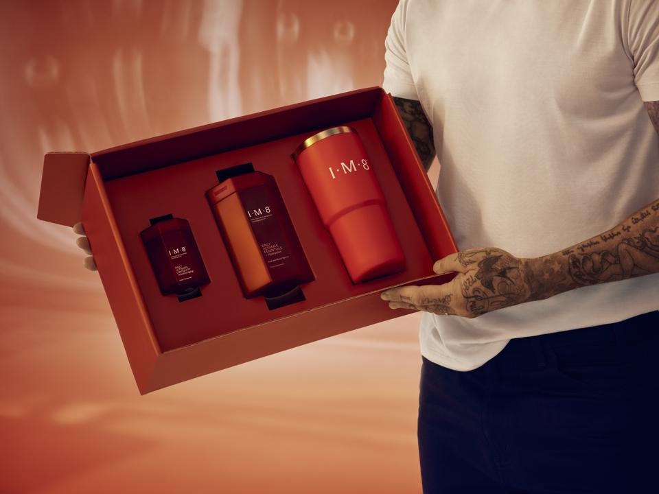 Hands holding an open IM8 Health gift box containing the Daily Ultimate Essentials tin, Longevity pack and branded tumbler.