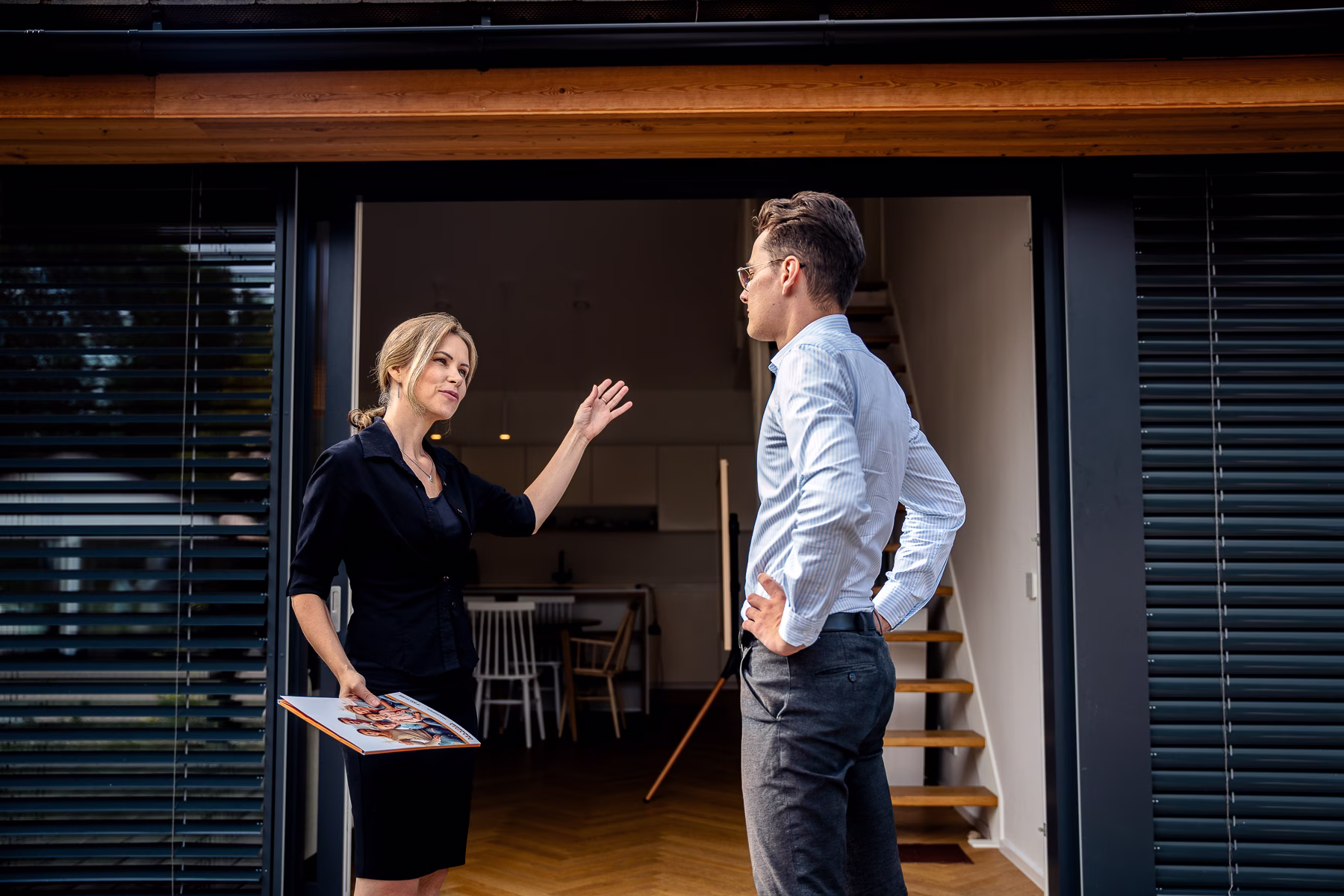 Žena stojící s mužem u otevřených dveří domu a diskutují o nemovitosti.