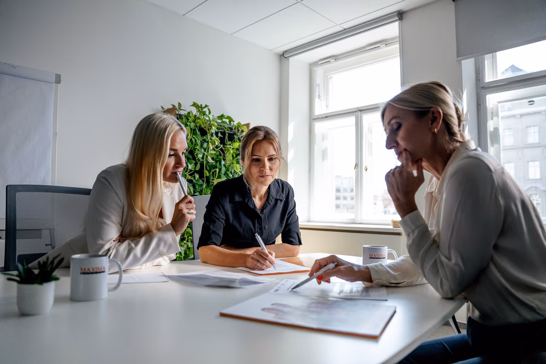 Tři ženy sedící u stolu a společně komunikují nad dokumenty.