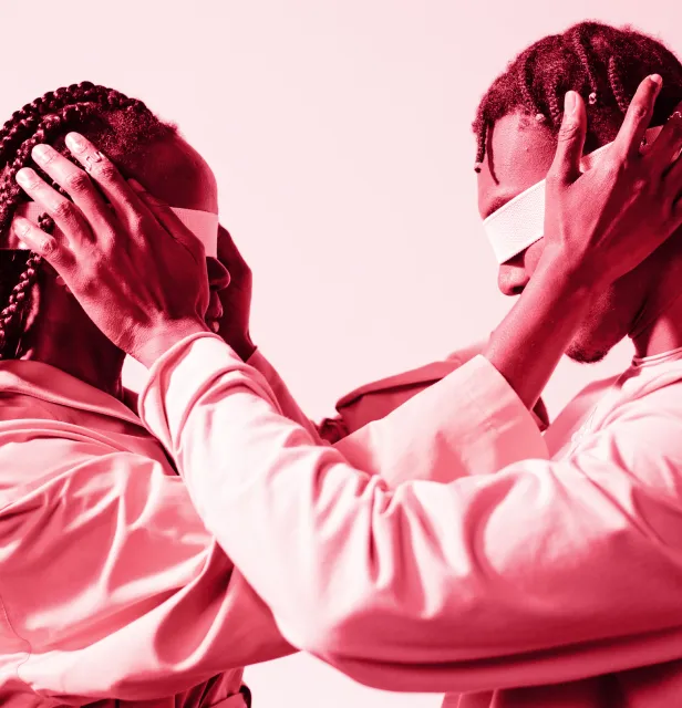 Two people facing each other with eyes covered by white blindfolds, gently holding each other's heads.