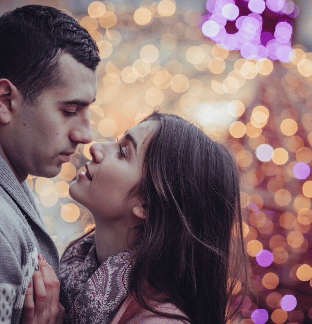 Couple looking into each other's eyes with blurred festive lights in the background.
