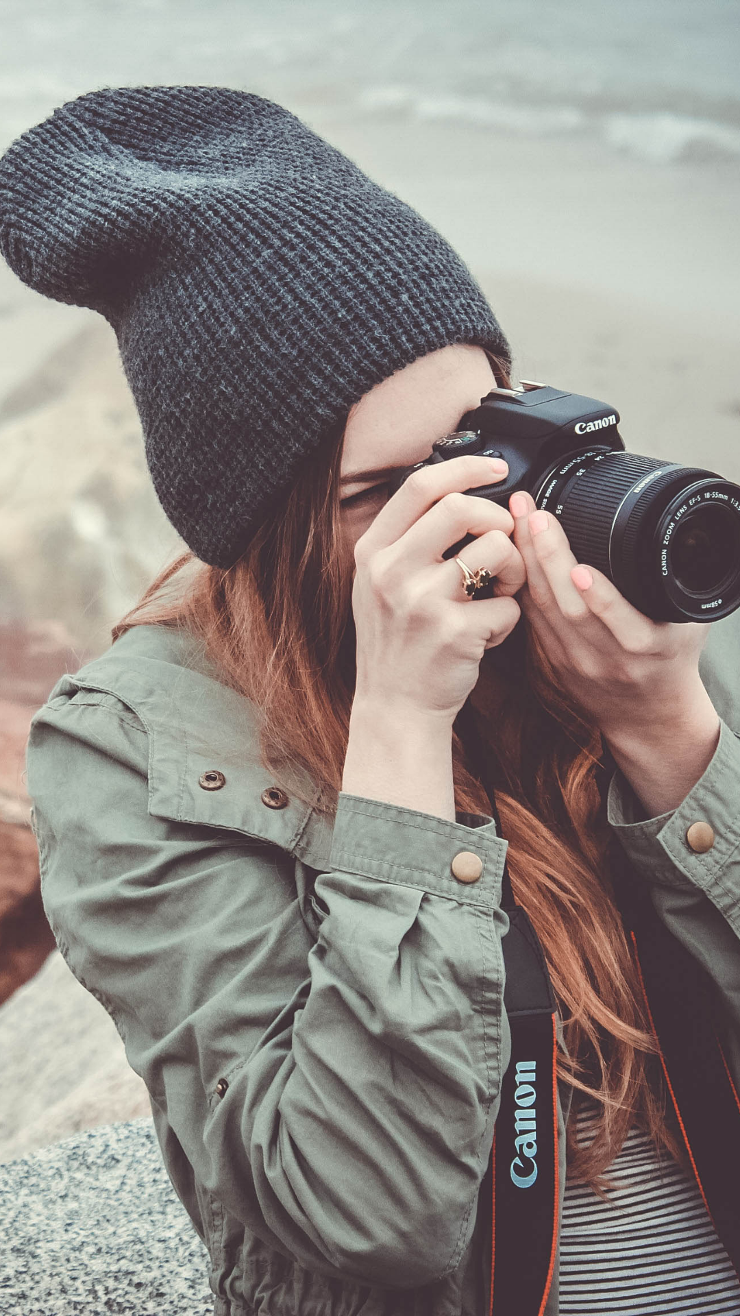 Person wearing a dark knit beanie and green jacket taking a photo with a Canon DSLR camera.