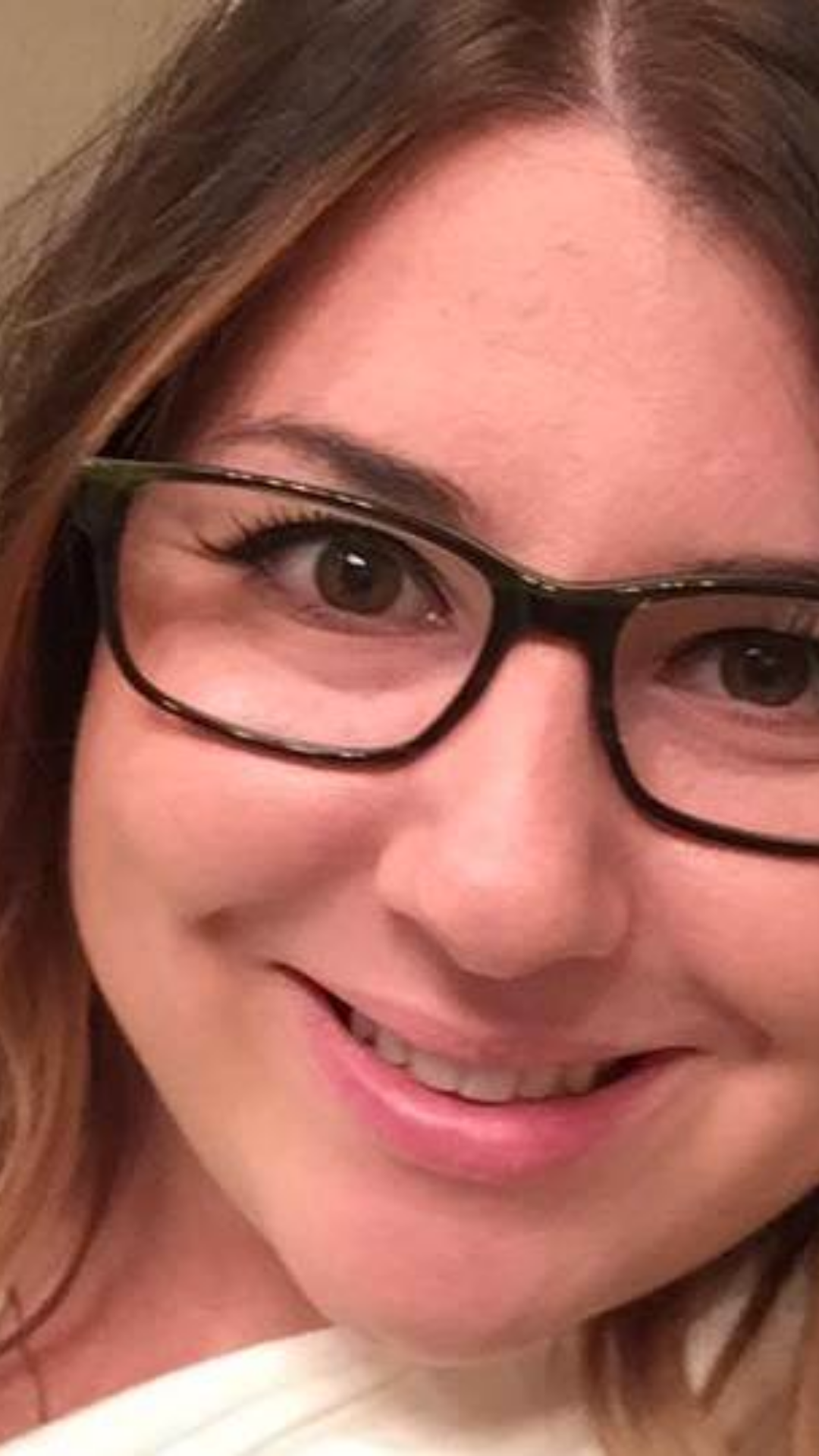 Close-up of a smiling woman with brown hair and black glasses.