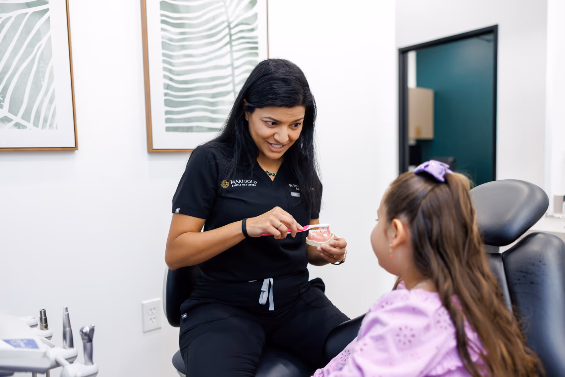 Dentist demonstrating proper toothbrushing on a dental model to a young girl in a dental office.