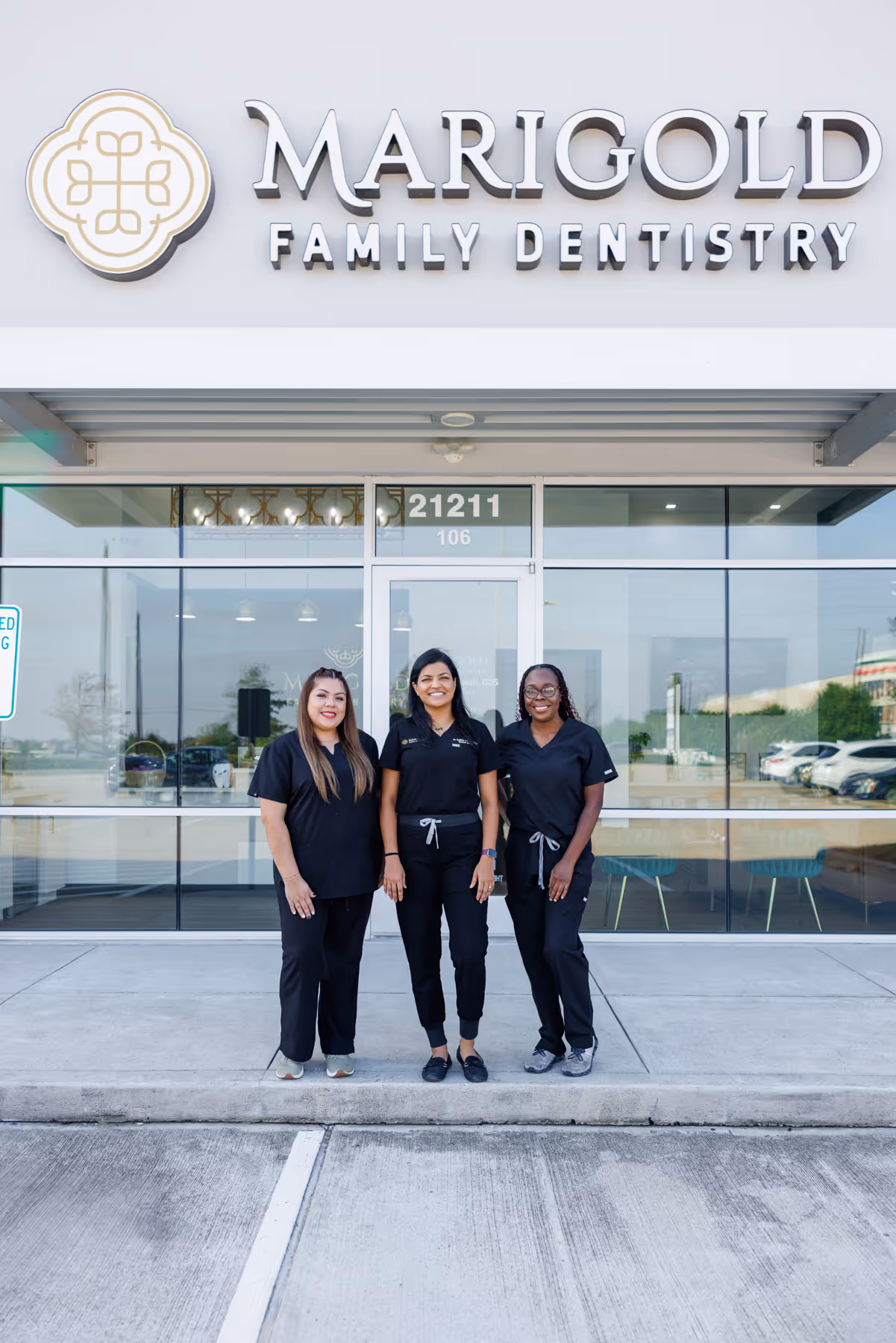 Three dental professionals wearing black scrubs standing outside Marigold Family Dentistry clinic.