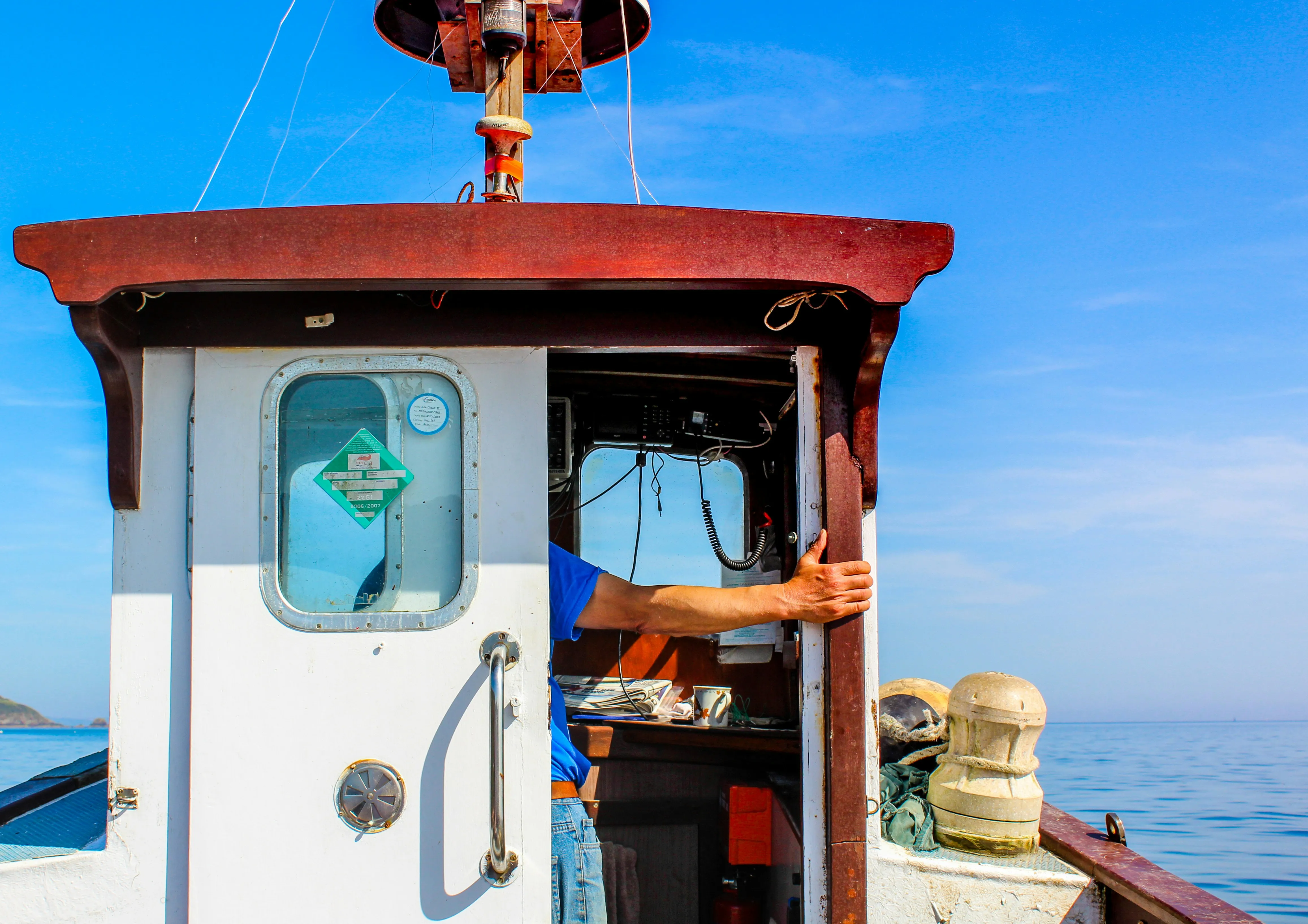 Fisherman standing in the doorway of a working fishing boat cabin at sea on a clear day.