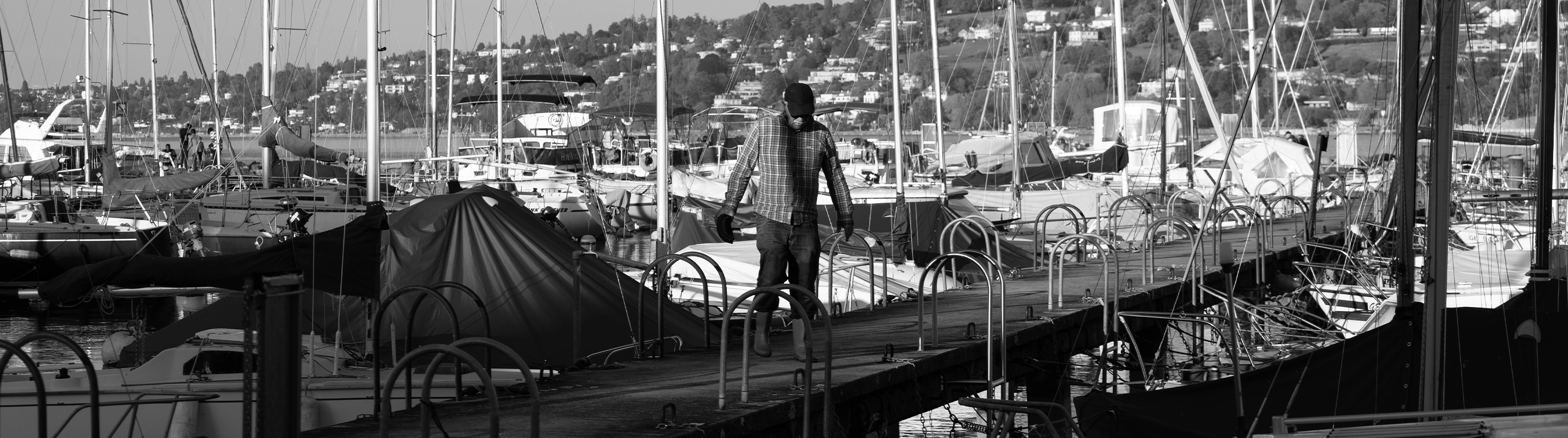 Fisherman walking along a marina dock surrounded by working boats and rigging in harbor.