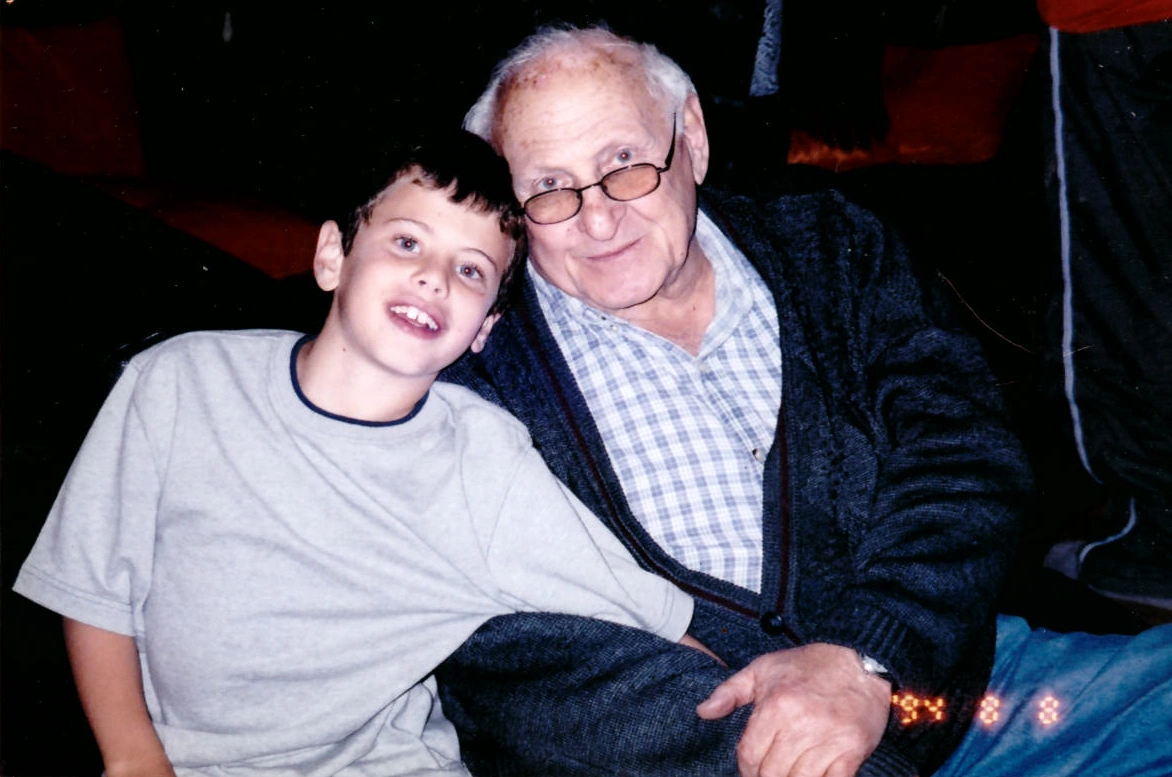 A young Ellie Hetz sitting beside his grandfather, smiling together.