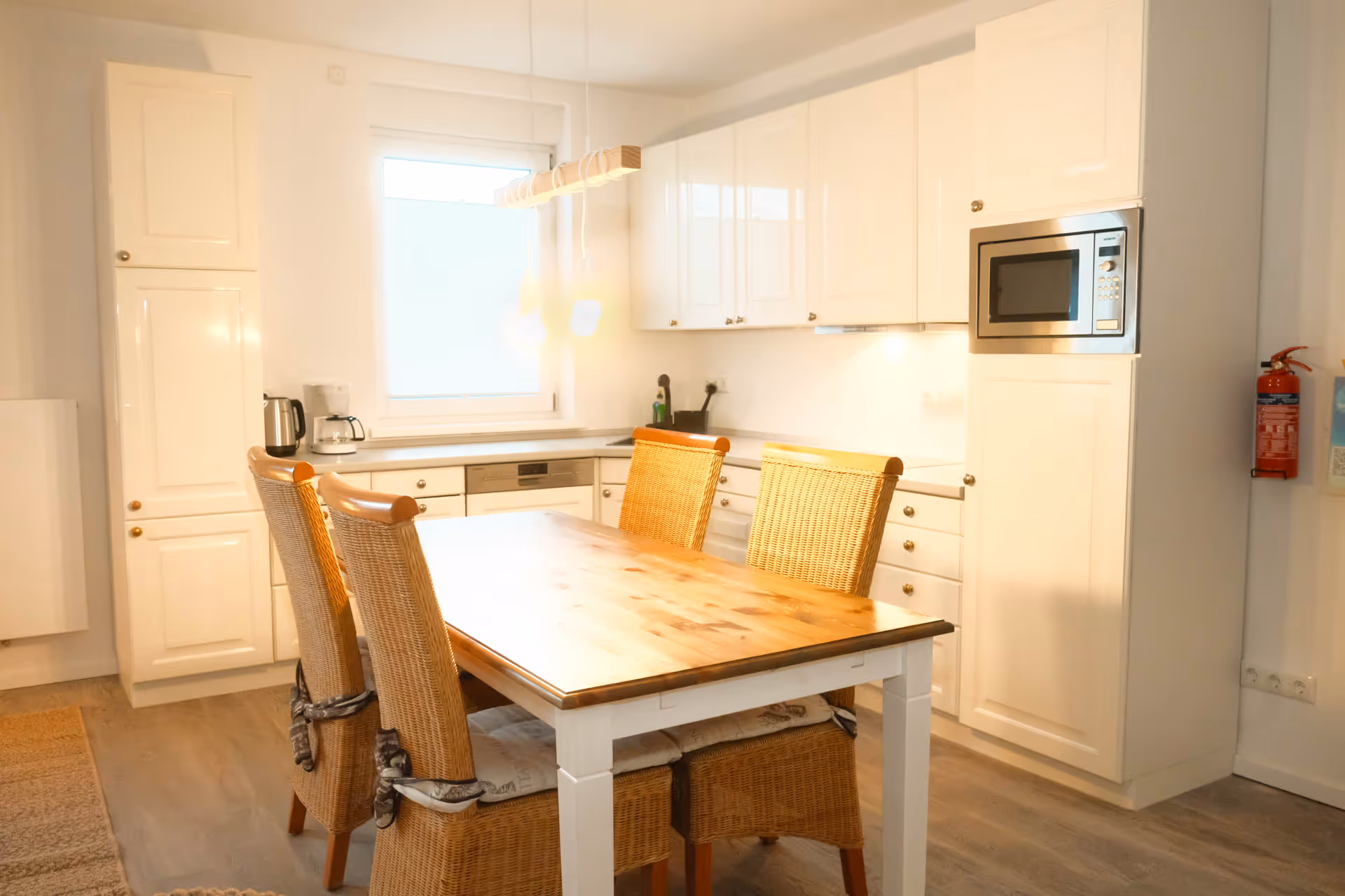 Weiße Einbaukueche mit Holztisch und Rattanstuehlen