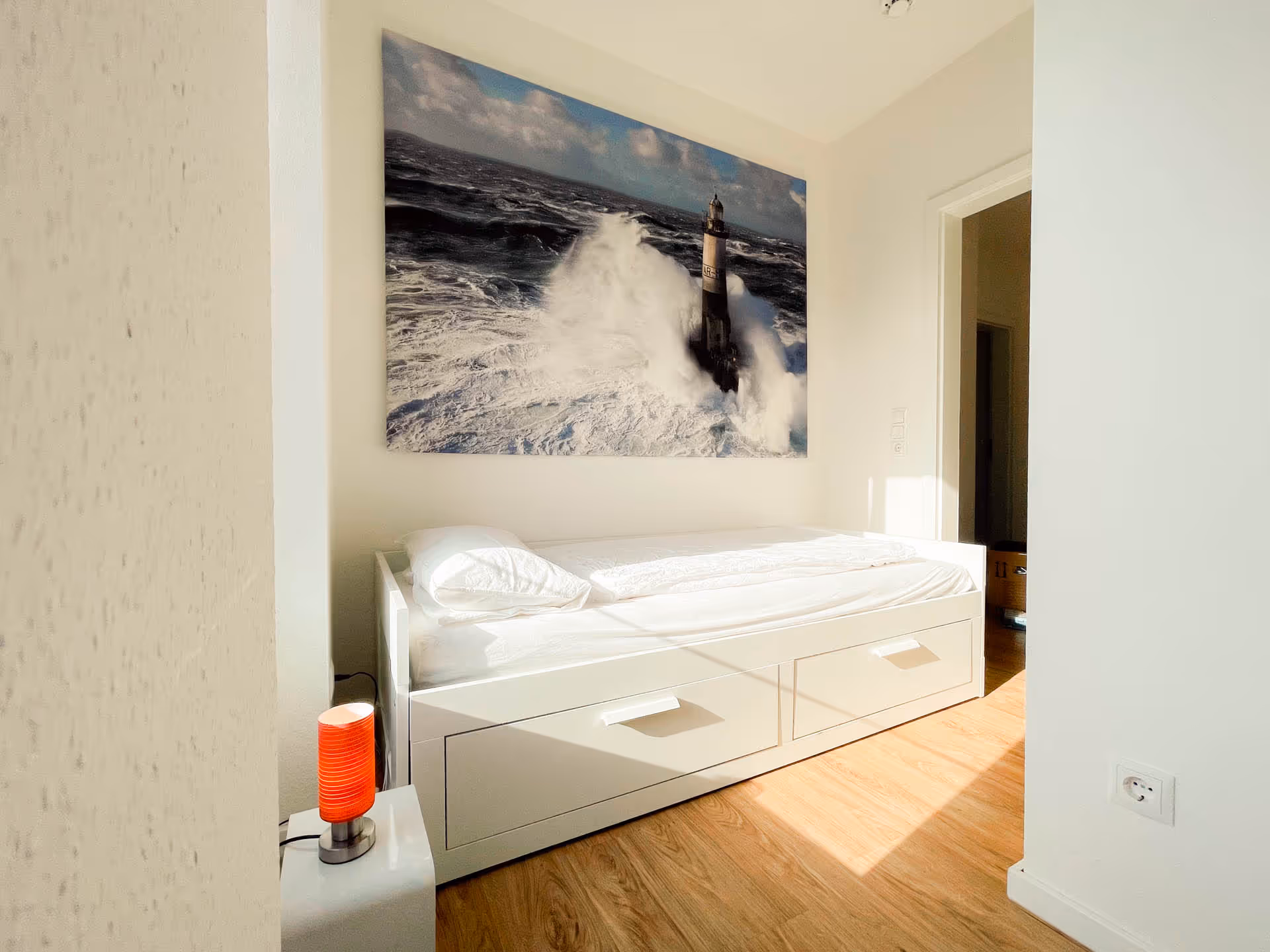 Einzelbett mit Leuchtturm-Bild an weißer Wand