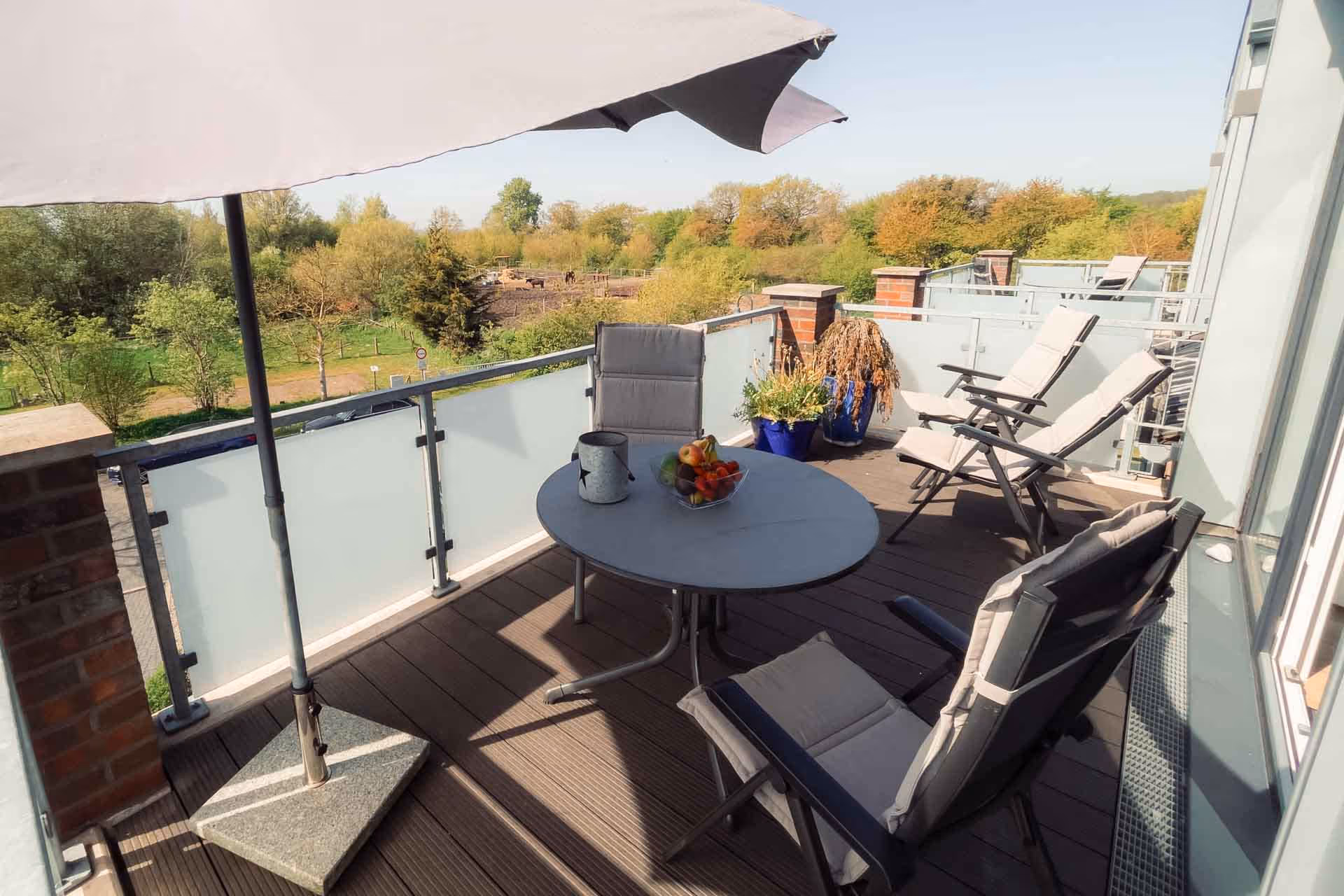 Großer Balkon mit Sitzgruppe und Sonnenschirm mit Blick ins Gruene