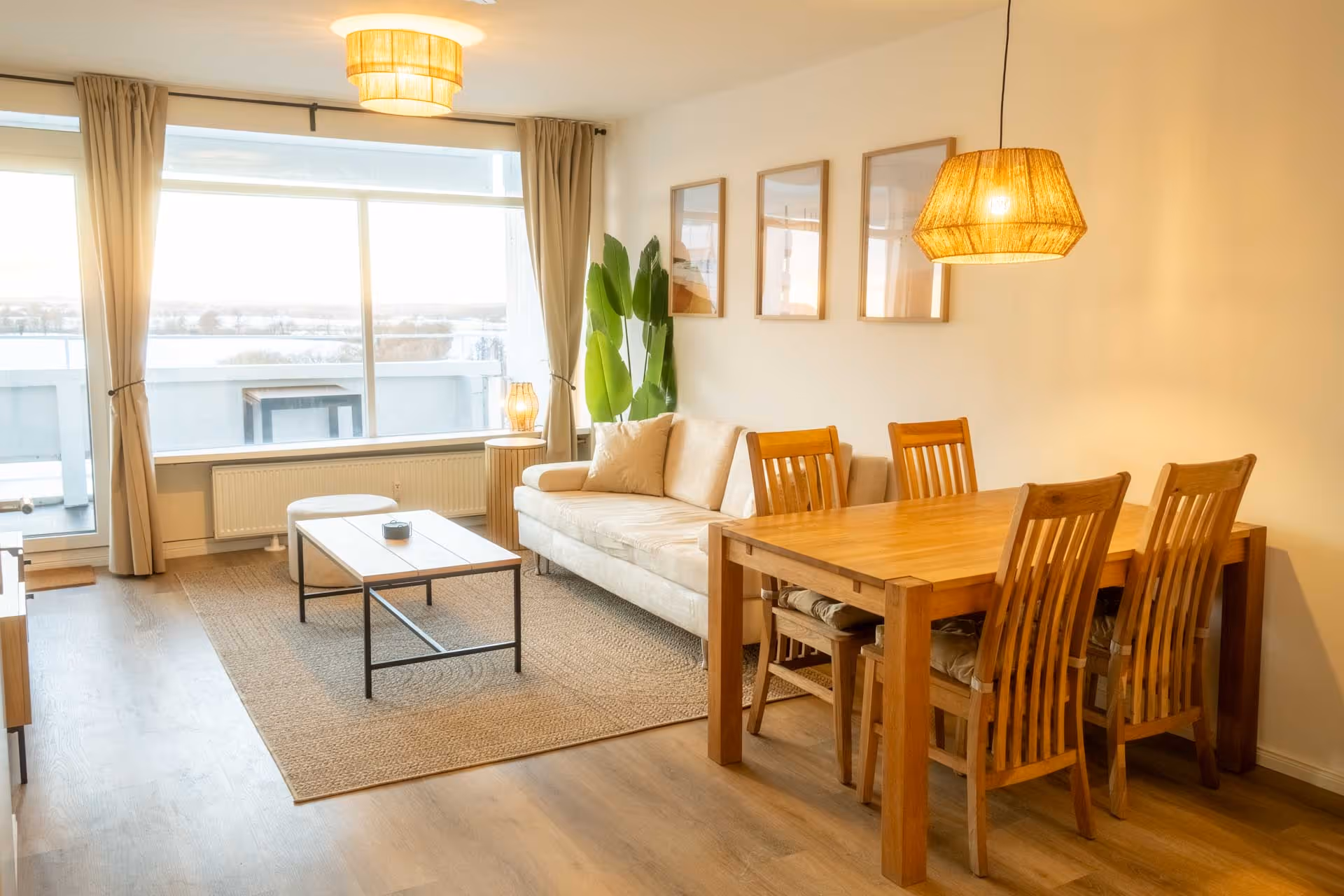 Heller Wohnbereich mit Sofa, Esstisch und Zugang zum Balkon