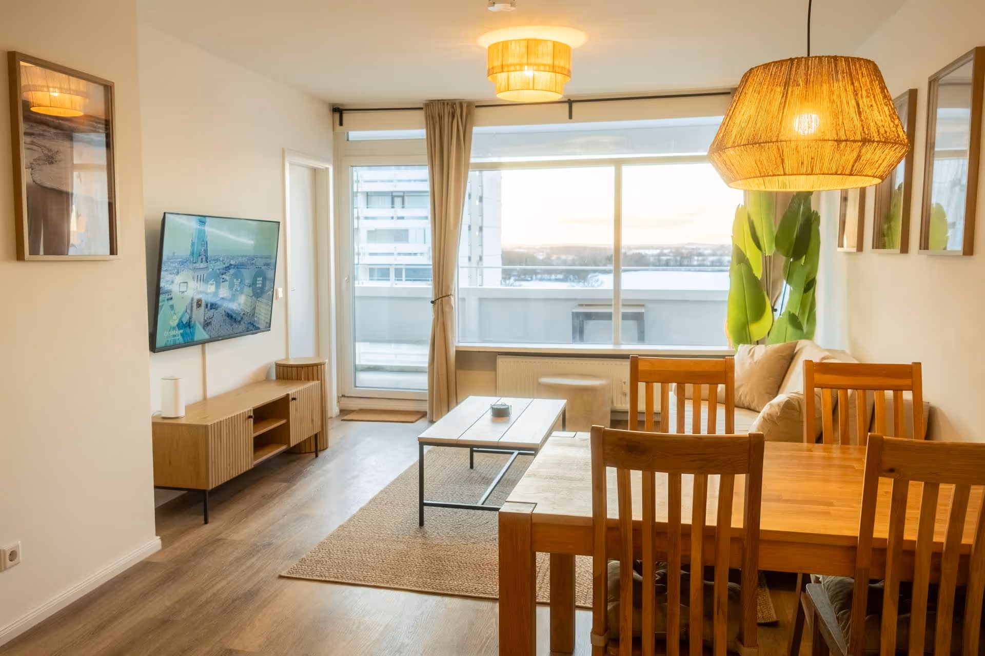 Wohnbereich mit Sofa, Esstisch, Fernseher und Balkonblick