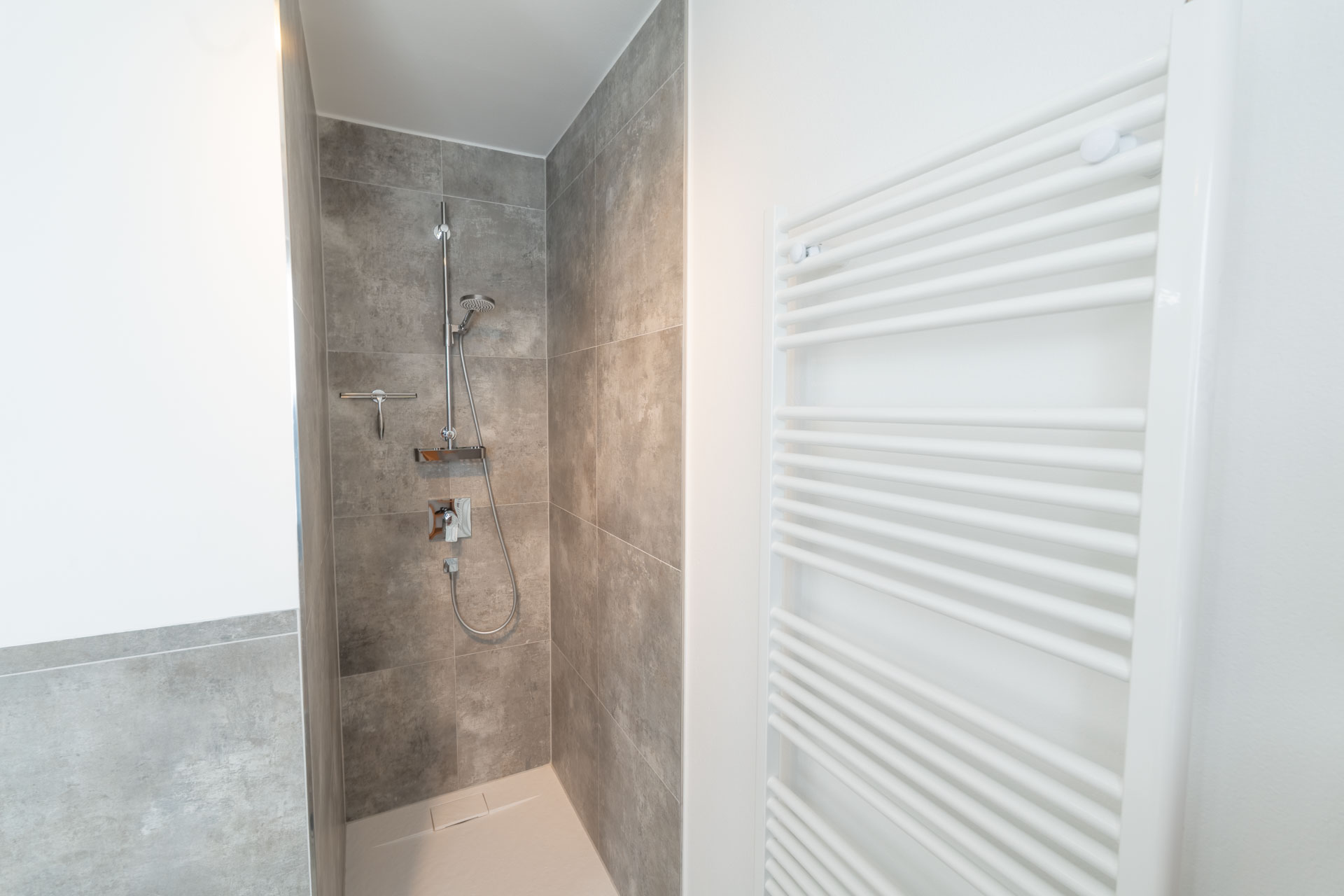 Dusche mit Handbrause und grauen Fliesen und Handtuchheizkörper