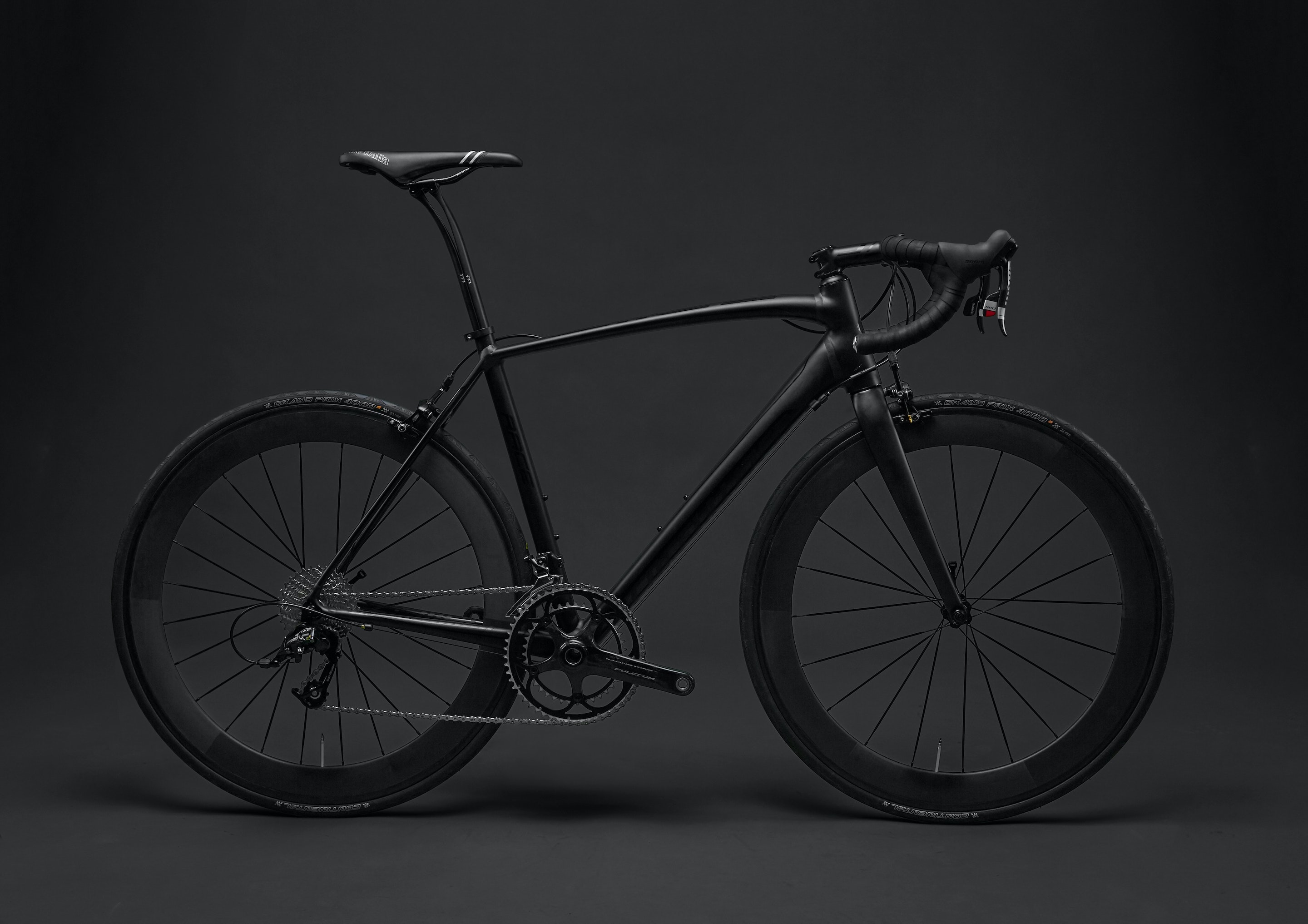 Sleek black road bicycle with drop handlebars and deep-section wheels on a dark background.