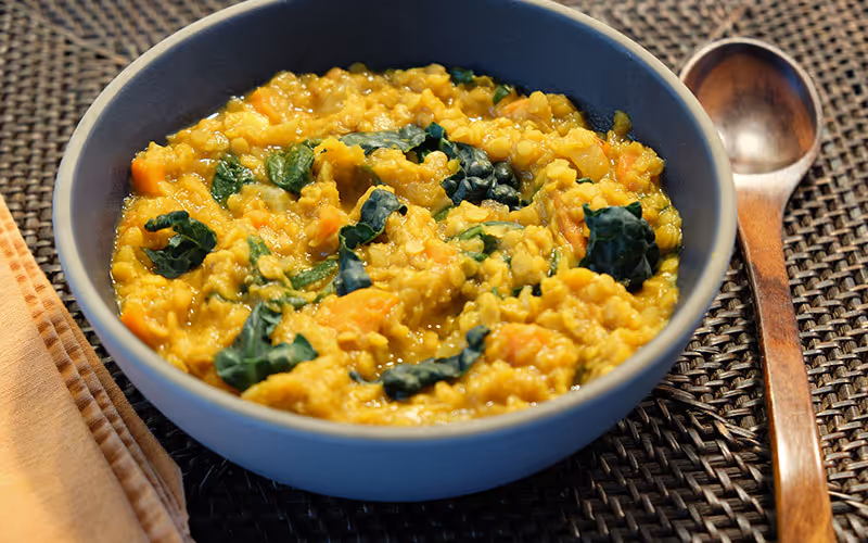 Red lentil soup with kale and carrots in a grey bowl with wooden spoon.