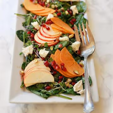 Persimmon and Apple Salad with Baby Greens and Pomegranate in a white bowl with fork