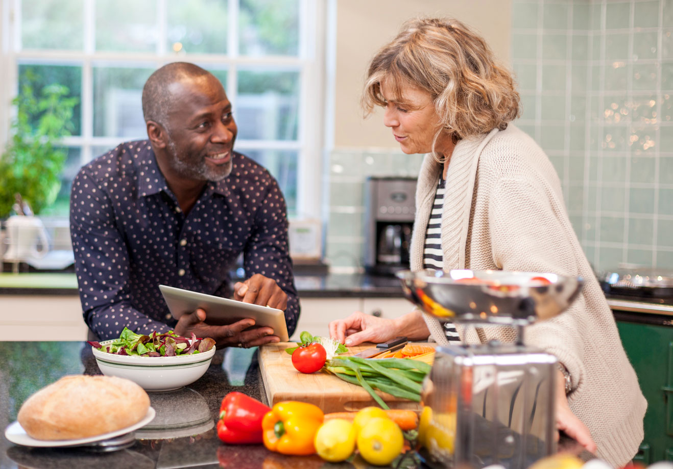 A senior multi-racial couple cooking together using the app.