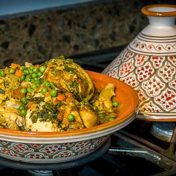 Traditional Moroccan chicken tagine with vegetables served in a decorative ceramic dish with a tagine lid nearby.