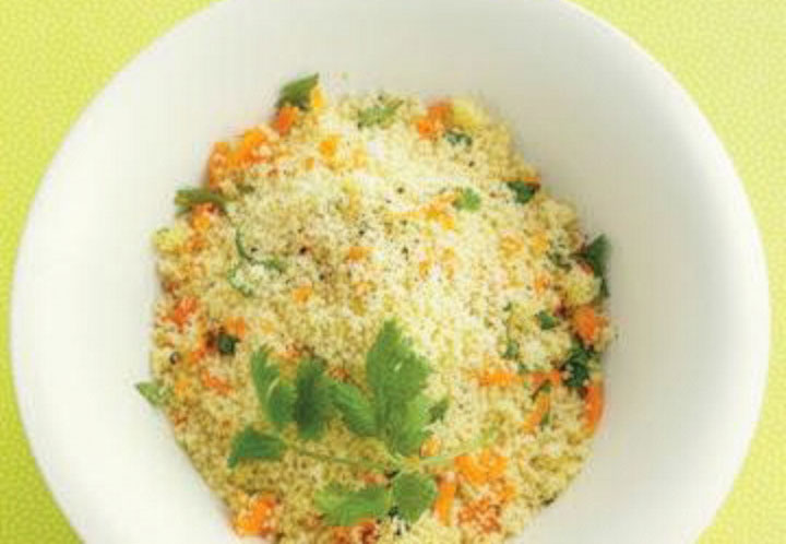 White bowl filled with couscous mixed with chopped carrots and cilantro leaves.