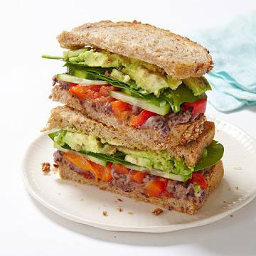 Veggie sandwich with lemony black bean spread, spinach, cucumber slices, and roasted red peppers on whole grain bread.
