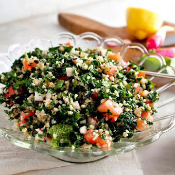 Glass bowl with fresh kale tabbouleh salad containing chopped kale, bulgur, tomatoes, herbs, and vinaigrette.