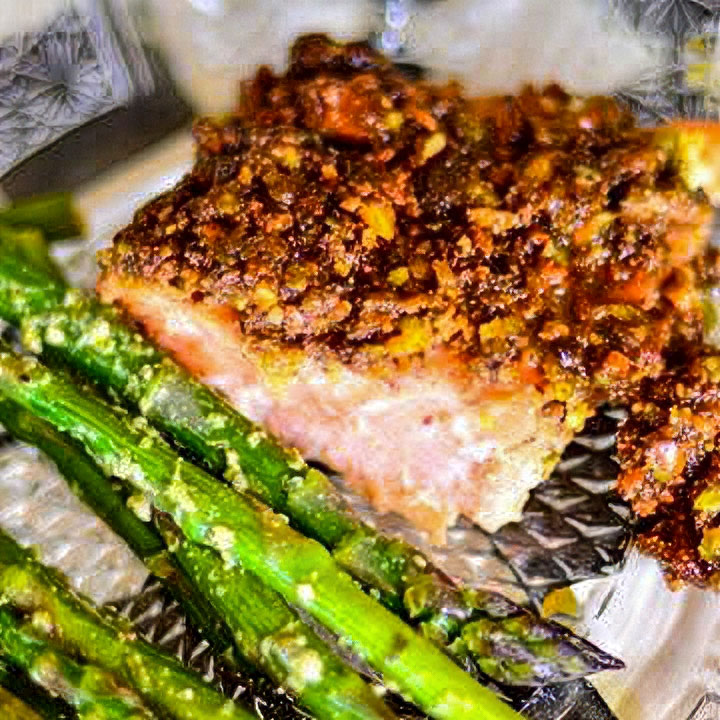 Close-up of a pistachio-crusted baked salmon fillet served with cooked asparagus.