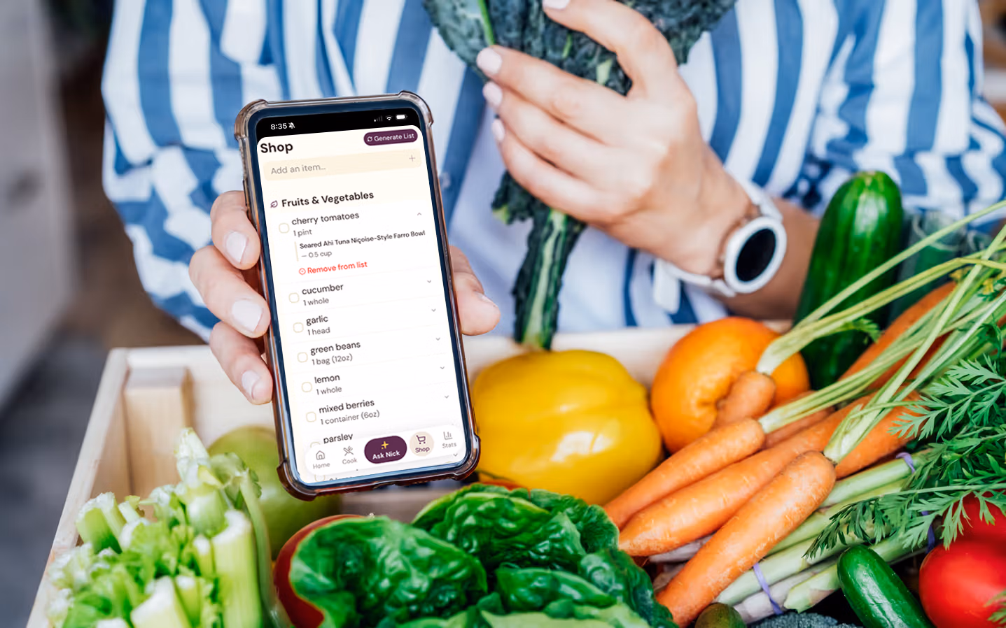 Person holding phone showing grocery list app with fresh vegetables in a crate.