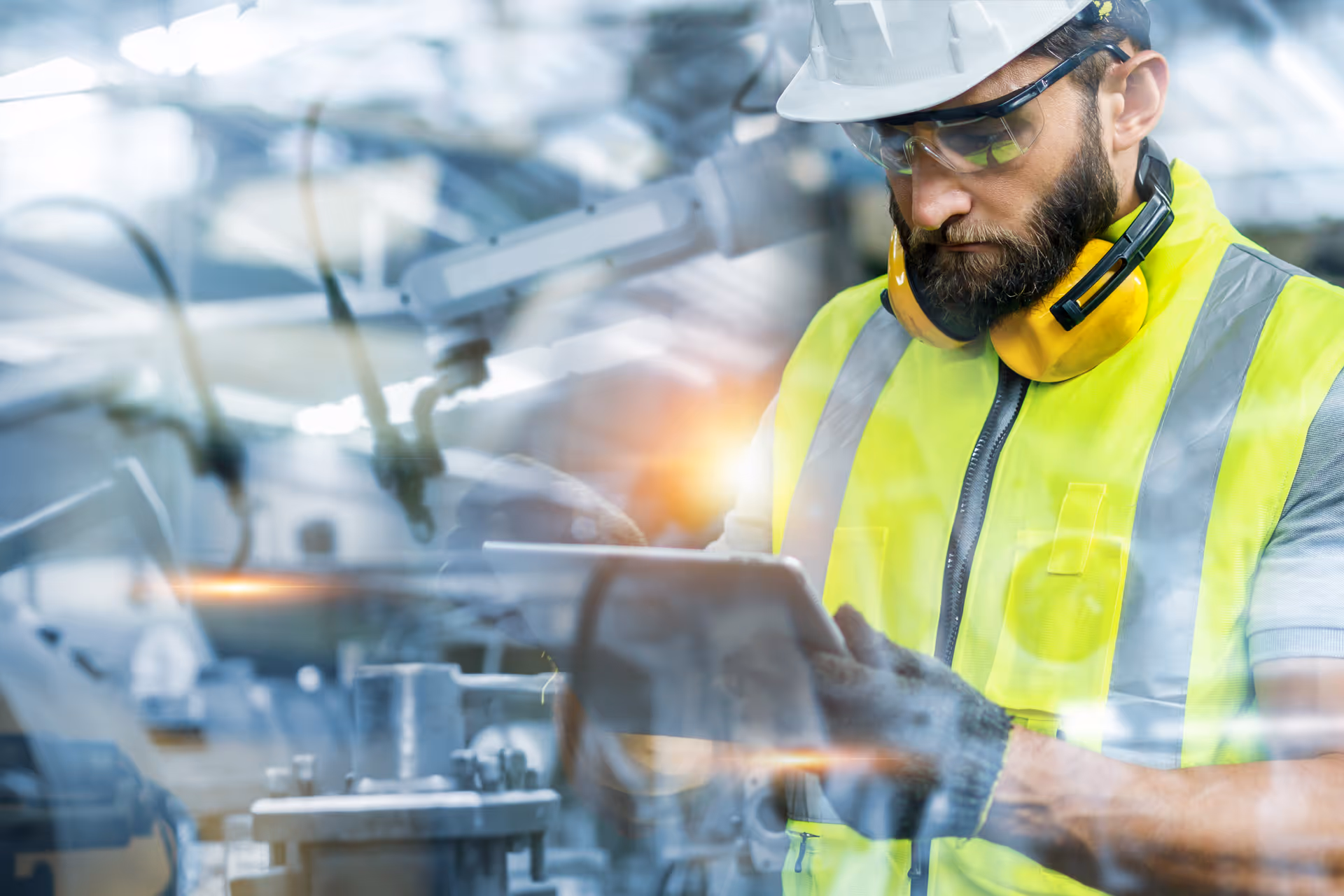 Engineer in safety gear using tablet while monitoring automated machinery, representing Wileo’s operational technology expertise