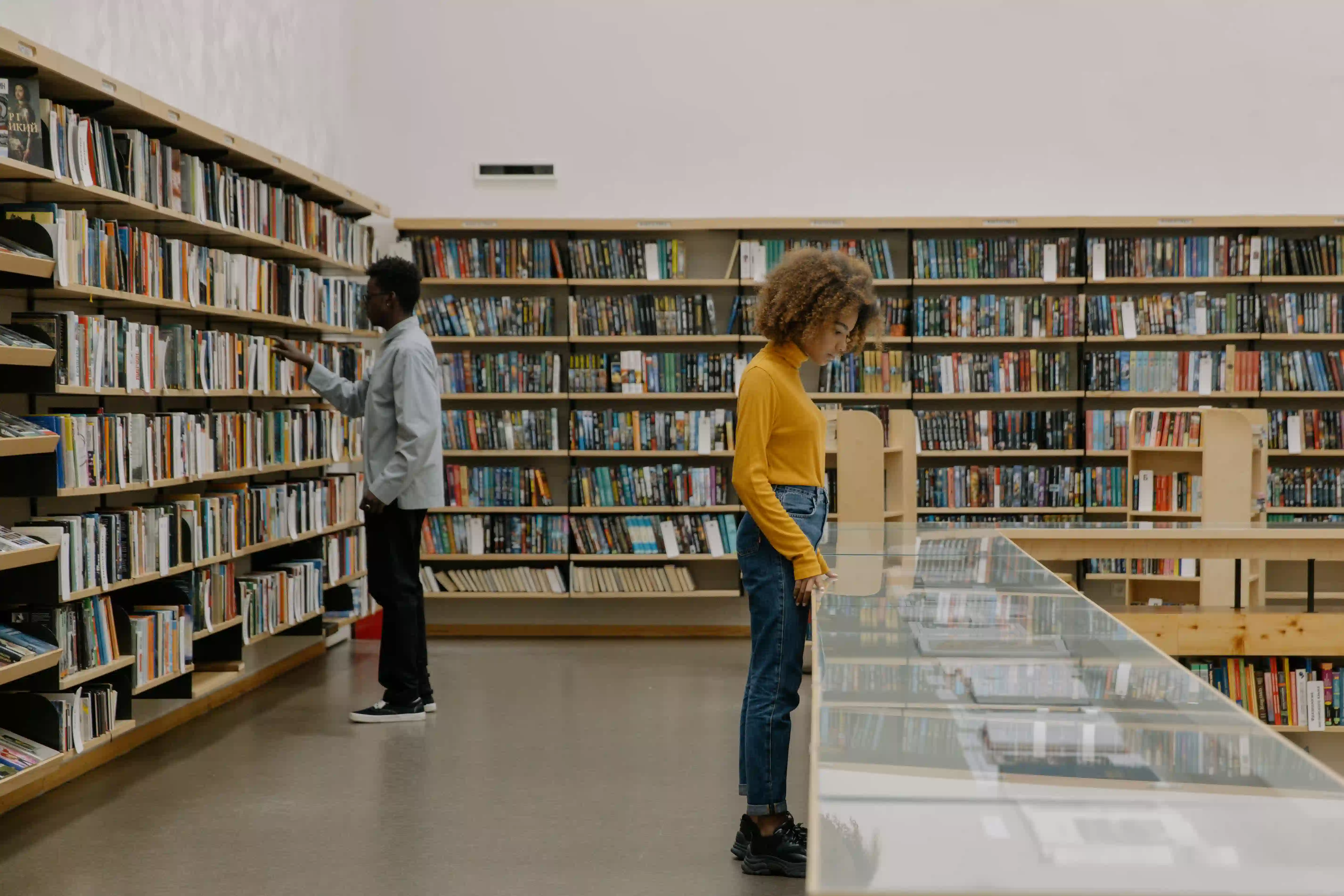 A man searching the stacks at a library. A woman reviewing an exhibit at a library.