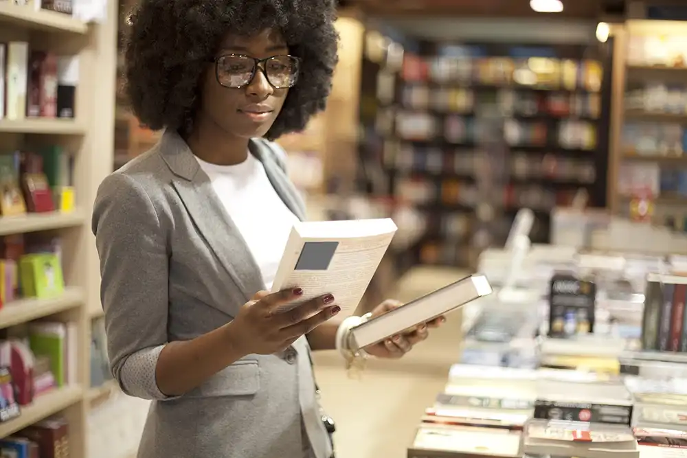 A woman scanning the front covers of two books at a bookstore.