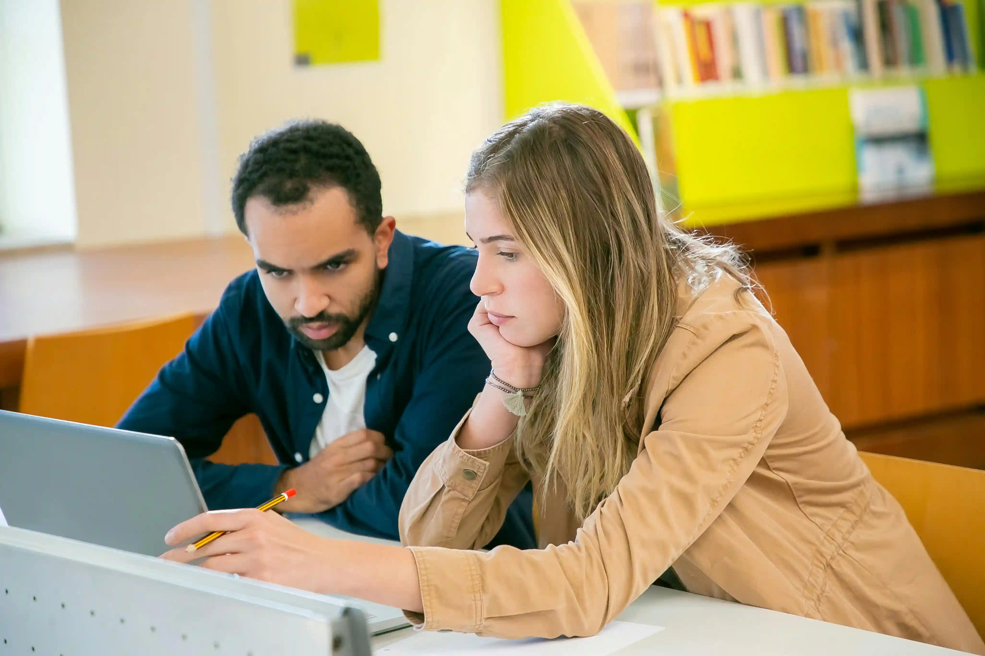Two students looking intently at a tablet in a library.
