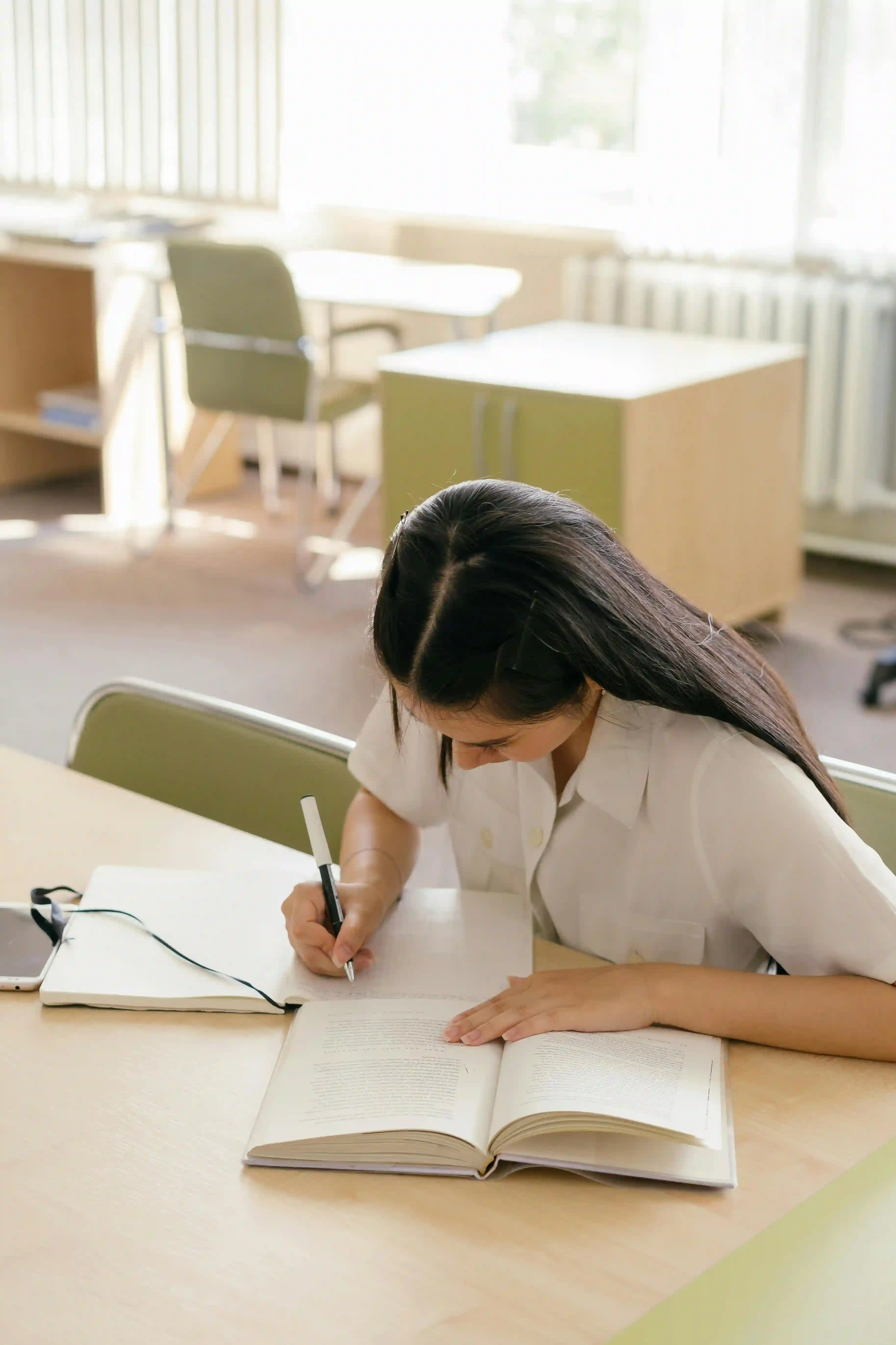 A mature student writing notes in a notebook on a book.