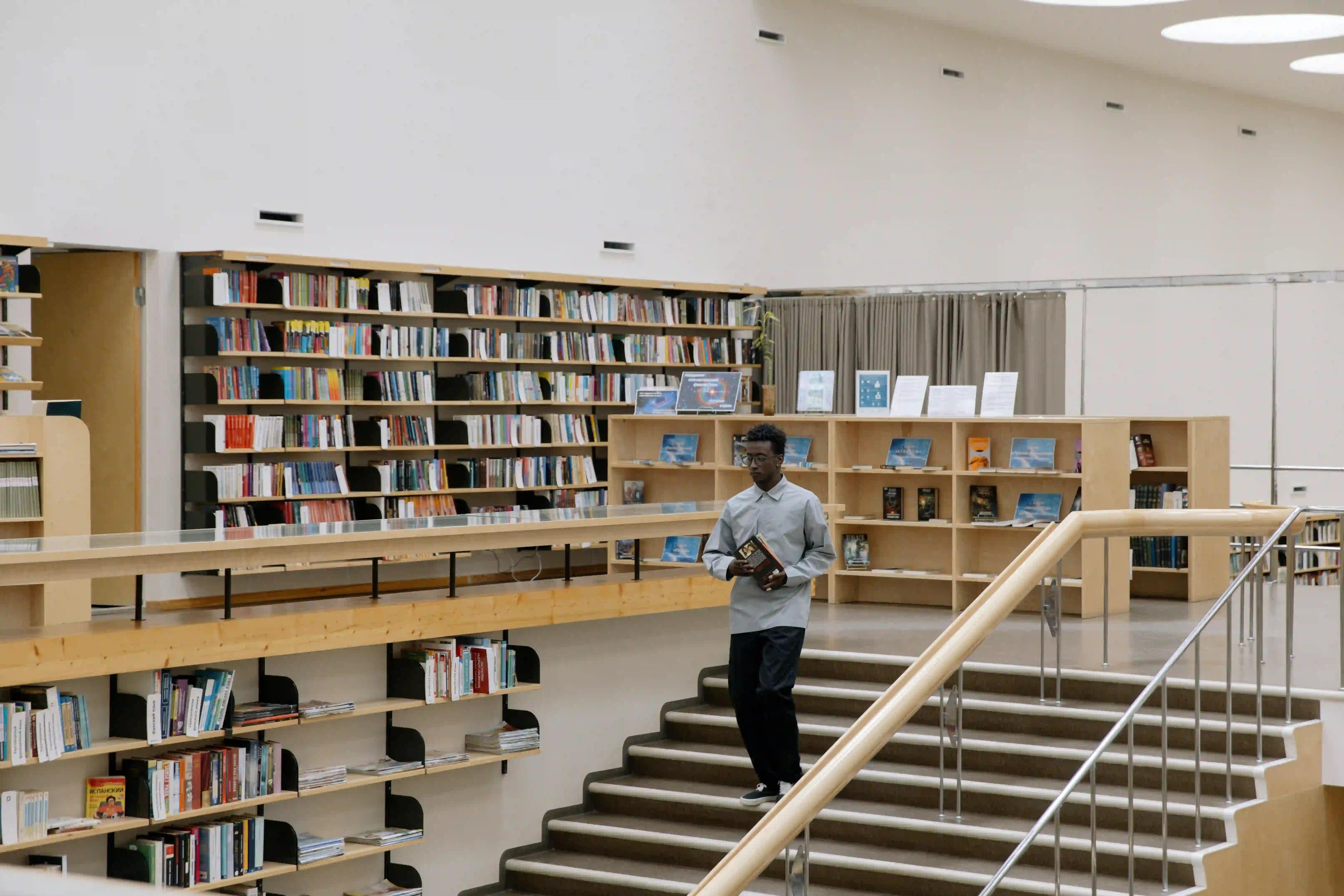 A young man walking down a staircase at a public library with a book in his hands.