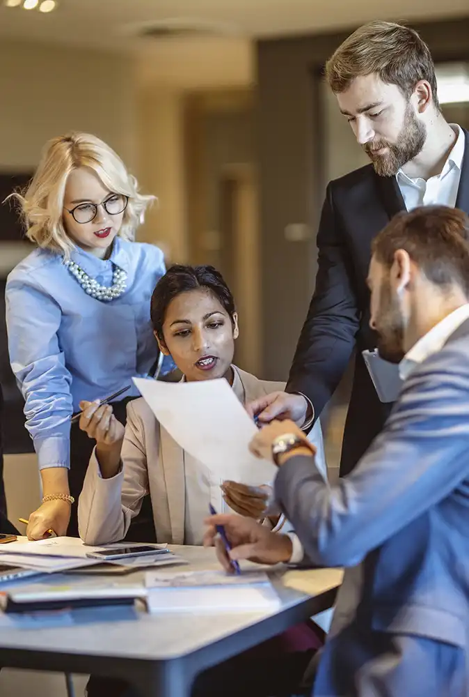 A group of business professionals discussing a document that one of them is holding up.