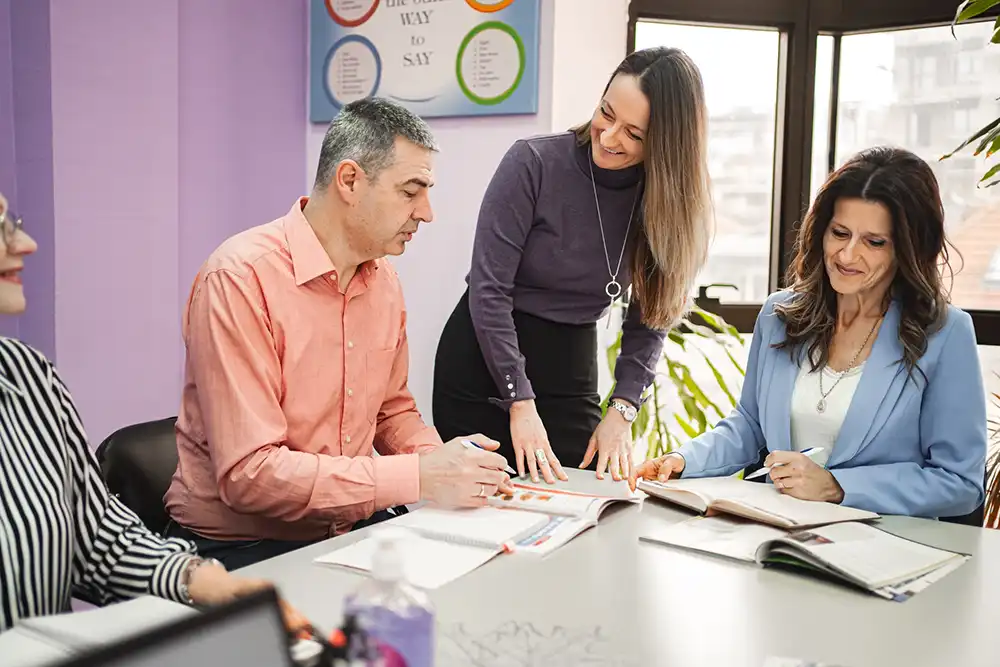 A teacher is talking to a mature student with other students seated next to them at a communal table.